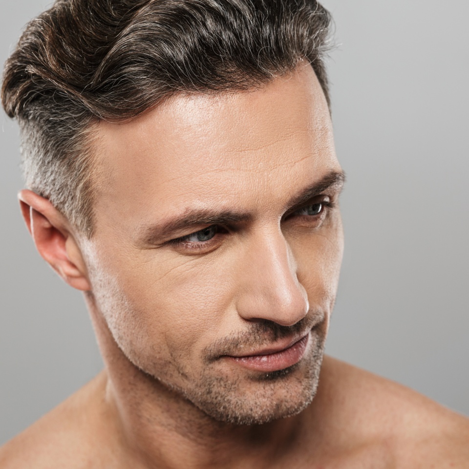 Picture of handsome serious mature man standing isolated over grey wall background naked. Looking aside.