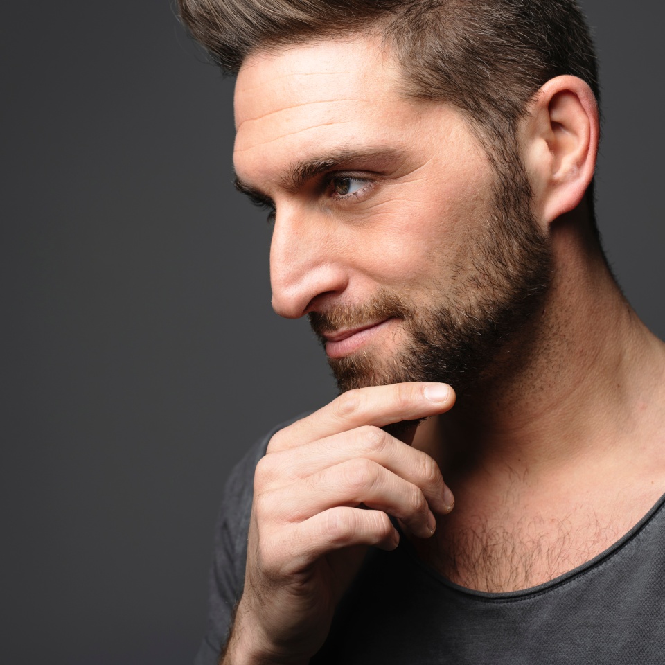 young man looking away while standing on dark background