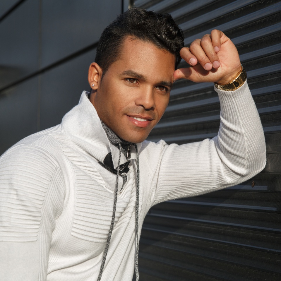 Portrait of a happy attractive Latino man with a smile on his face in stylish white casual clothes on a black background outside.