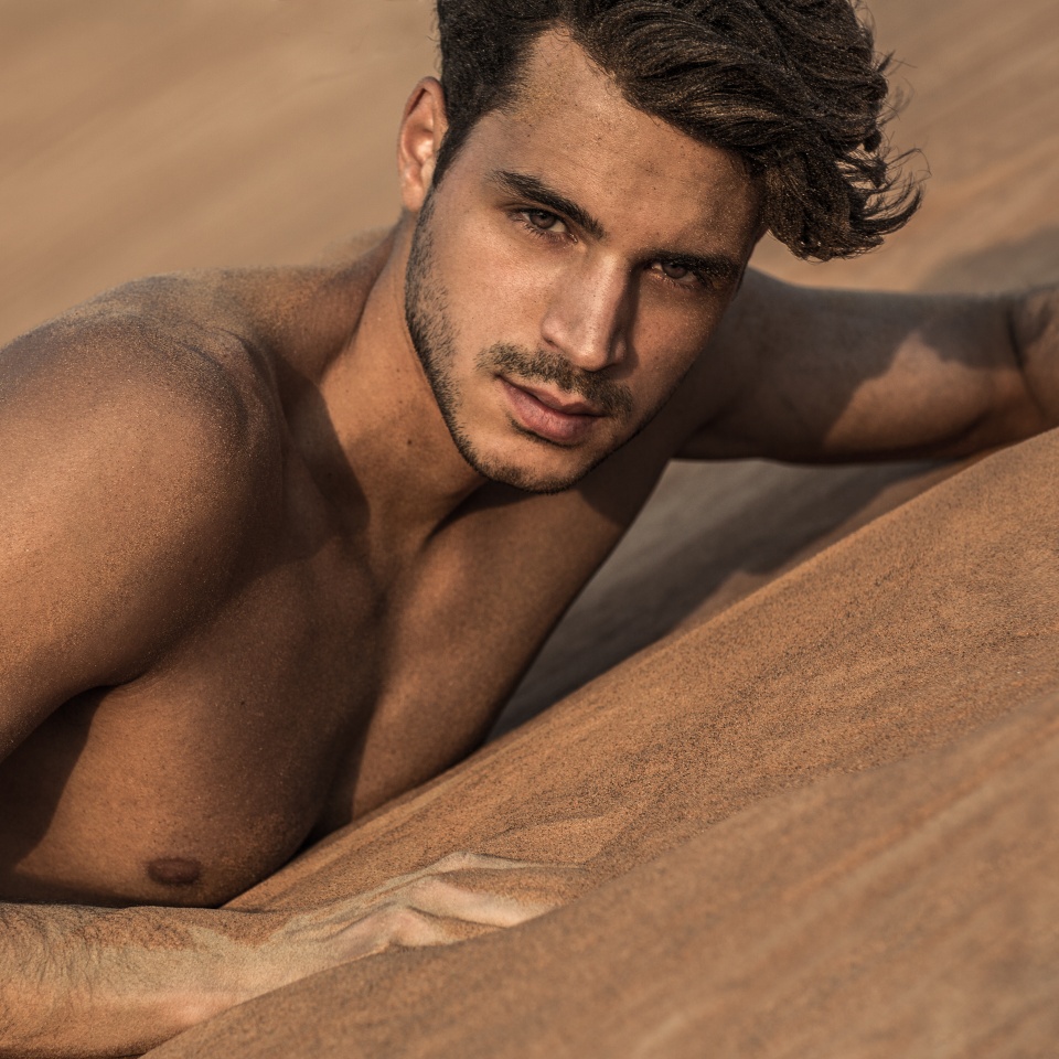 Sexy handsome topless male model lying on the desert sand. Beauty portrait.