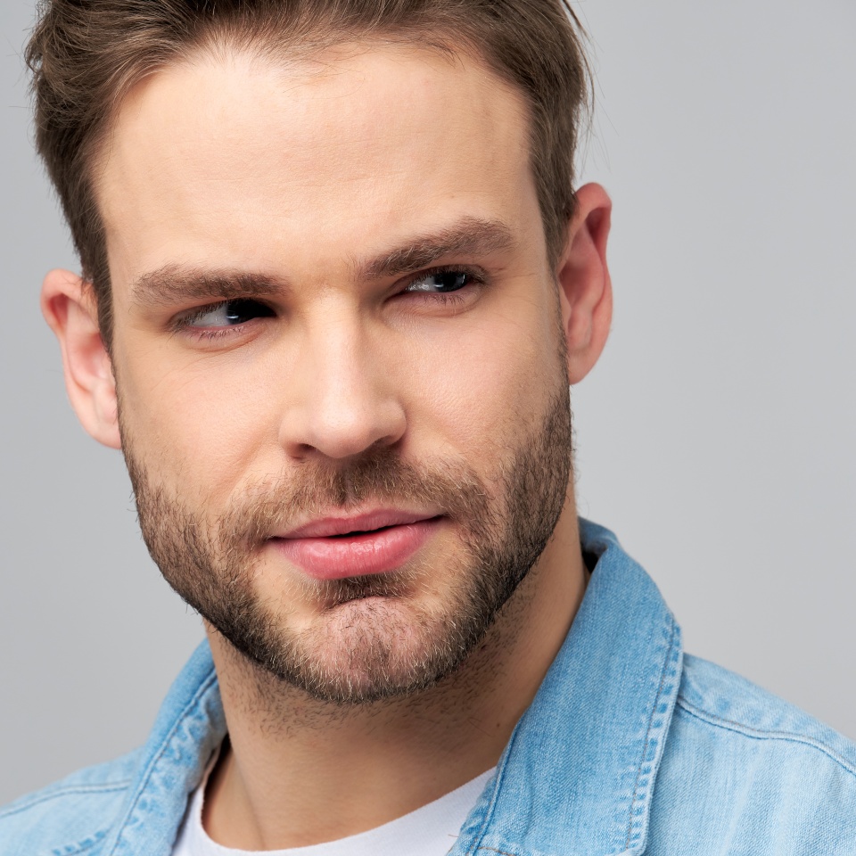 Close-up Portrait of young handsome caucasian man in jeans shirt over light background