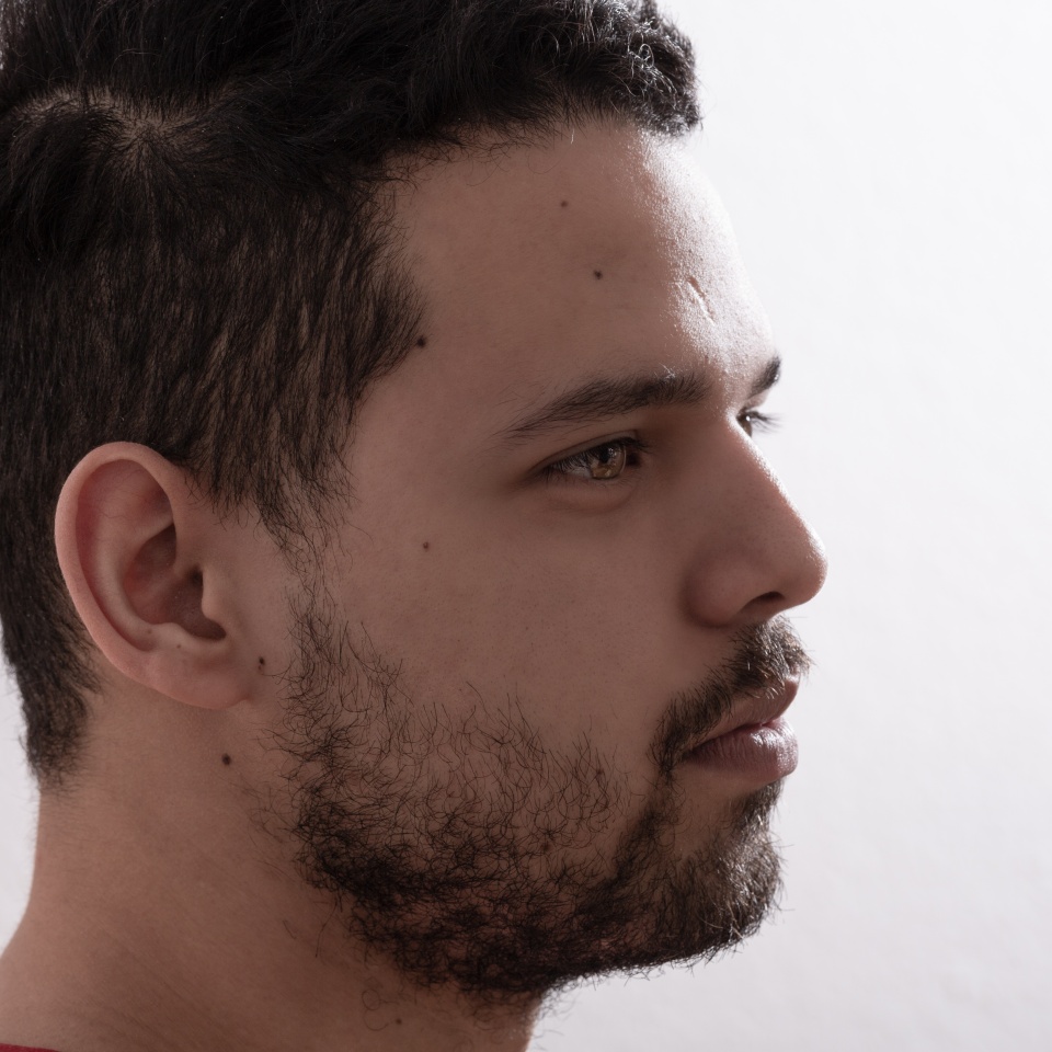 Extreme closeup of a young man profile. He is a Latino in his 20s and he is serious looking forward.