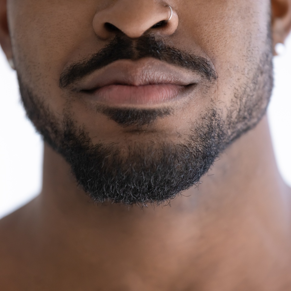 Close up of groomed beard of multiracial African guy with nose piercing lower face with trimmed black stylish stubble. Male beauty care grooming barber work concept