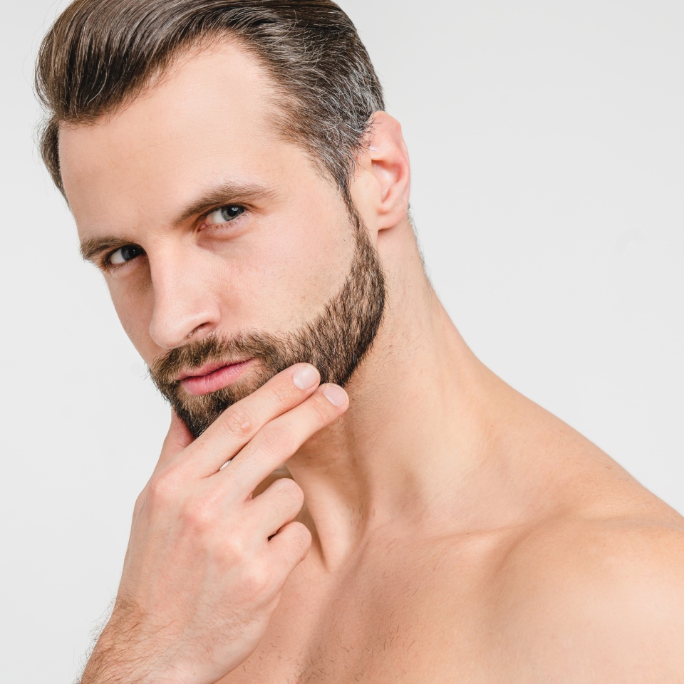 Closeup portrait of serious pensive caucasian attractive young shirtless naked man looking at camera touching his unshaven face, wants to use razor for barber shop care isolated in white background