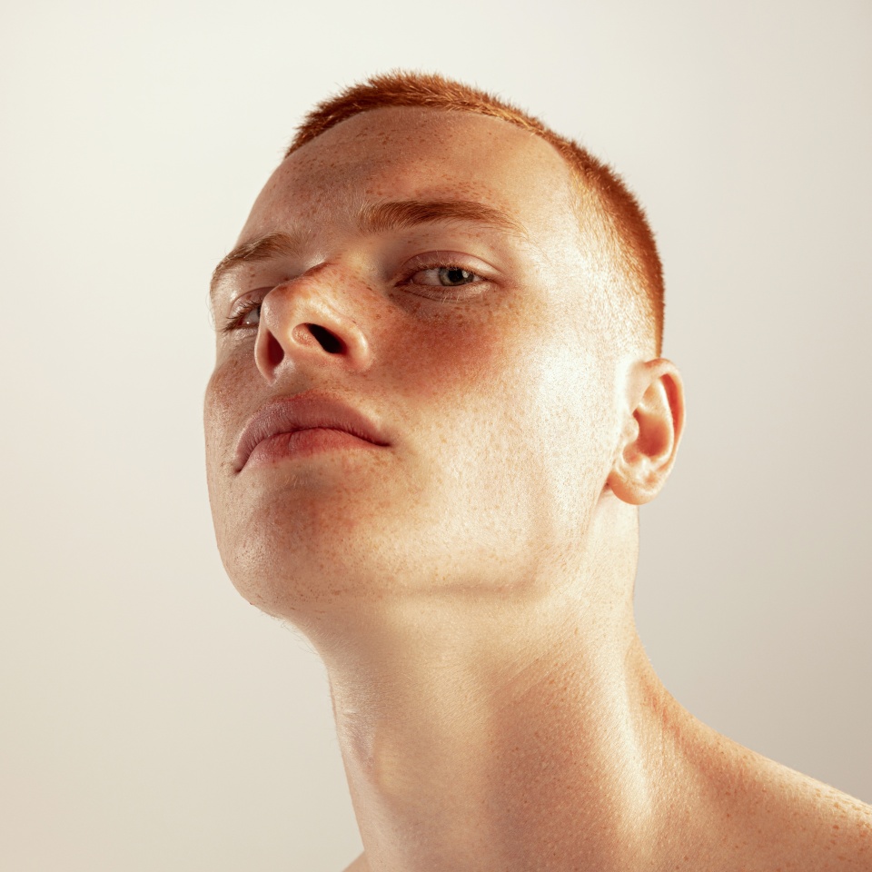 Close-up portrait of young red-haired freckled man posing isolated over grey studio background. Concept of men's health, lifestyle, beauty, body and skin care. Model looking at camera