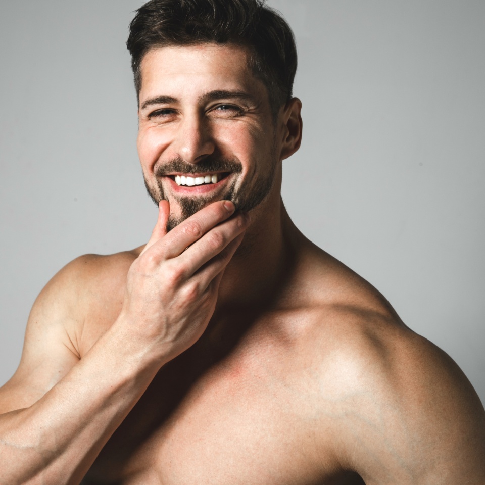 Portrait of a smiling handsome young man with a stylish haircut posing over gray background. Perfect body and skin. Studio shot.