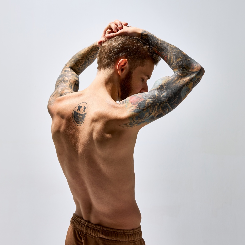 Portrait of muscular male fashion model posing isolated over grey studio background. Man posing shirtless. Masculinity. Concept of men's health, beauty, body and skin care, fitness. Body art
