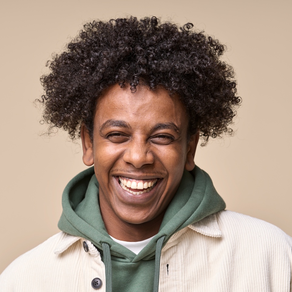 Happy cheerful young African American gen z guy isolated on beige background. Smiling funny ethnic teen student, cool curly generation z teenager laughing with white perfect teeth, close up portrait.