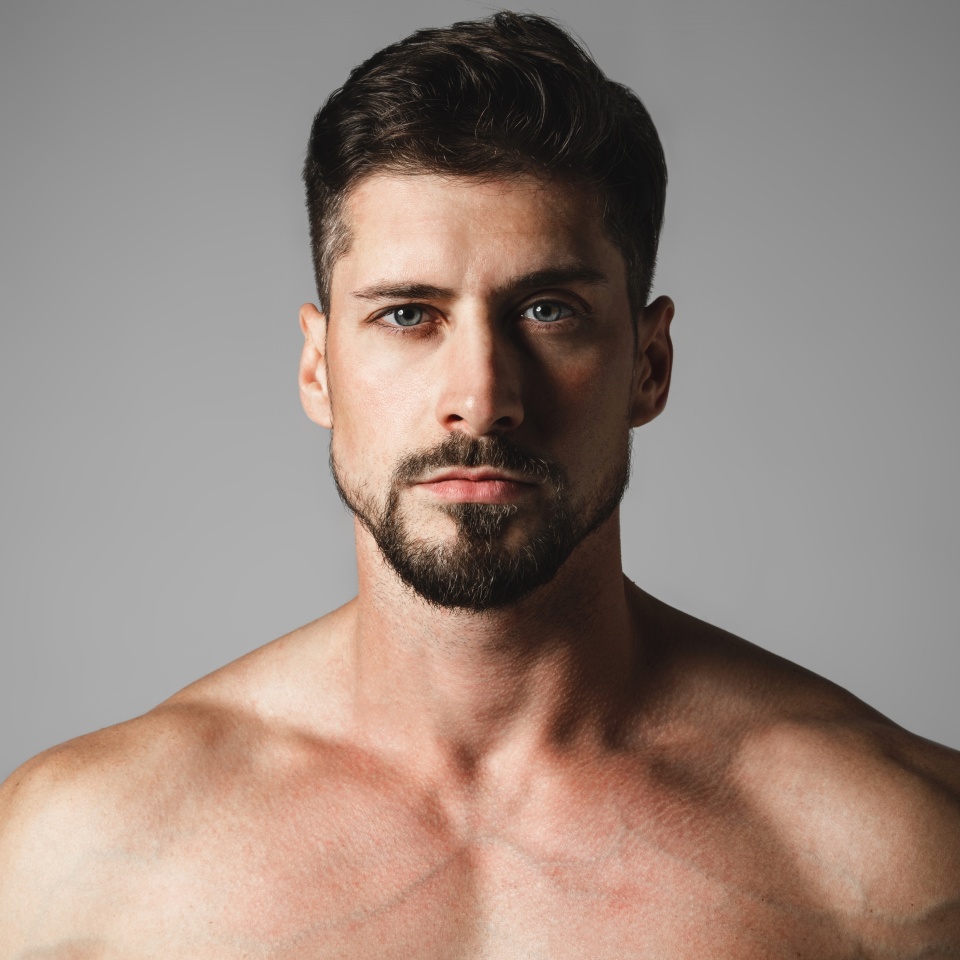 Portrait of a handsome young man with a stylish haircut posing over gray background. Perfect body and skin. Studio shot.