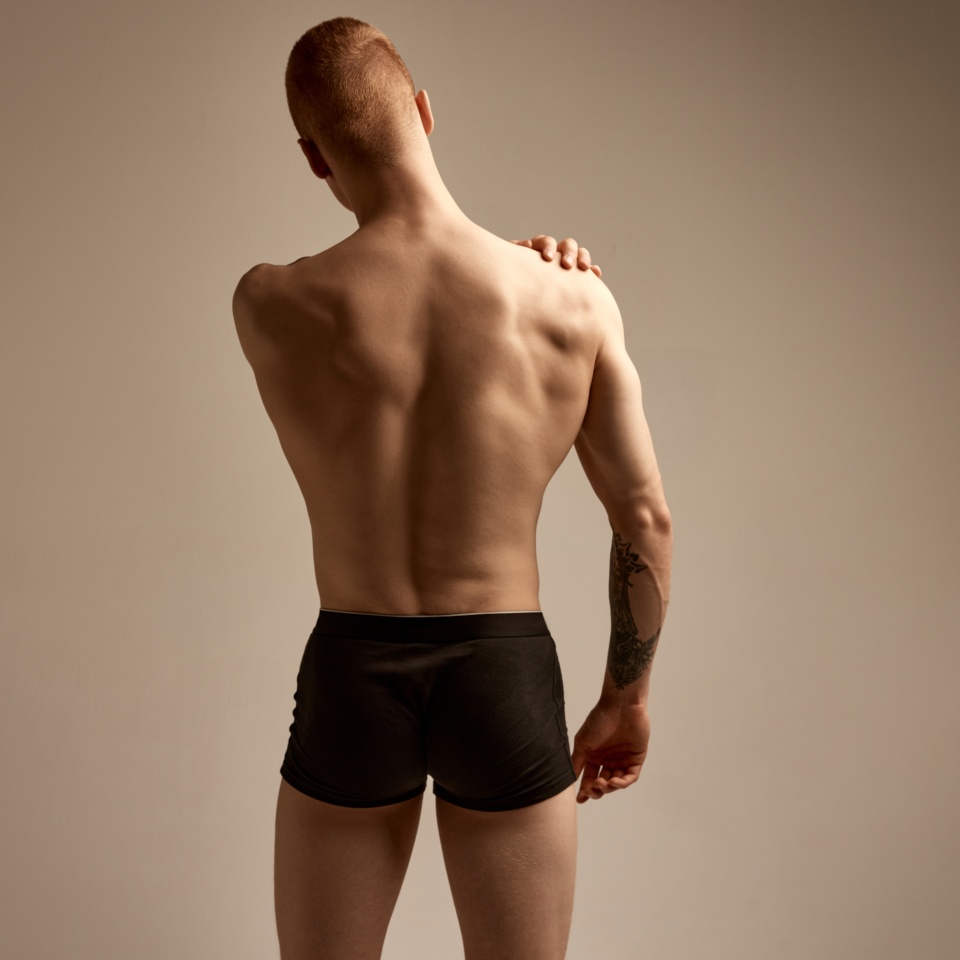 Back view. Young redhead boy posing in black boxers, underwear over beige studio background. Strong, relief body shape. Concept of men's health and beauty, body and skin care, fitness. Body art