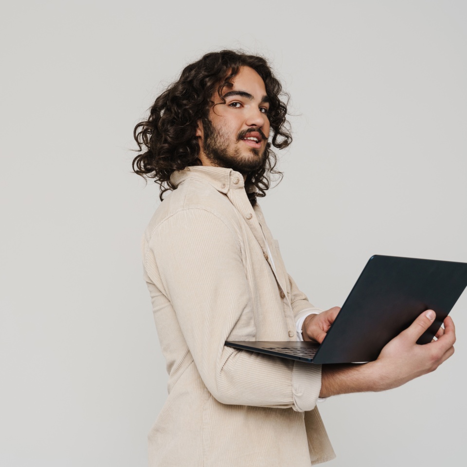 Young smiling hispanic man with long curly hair working on laptop isolated over white studio background