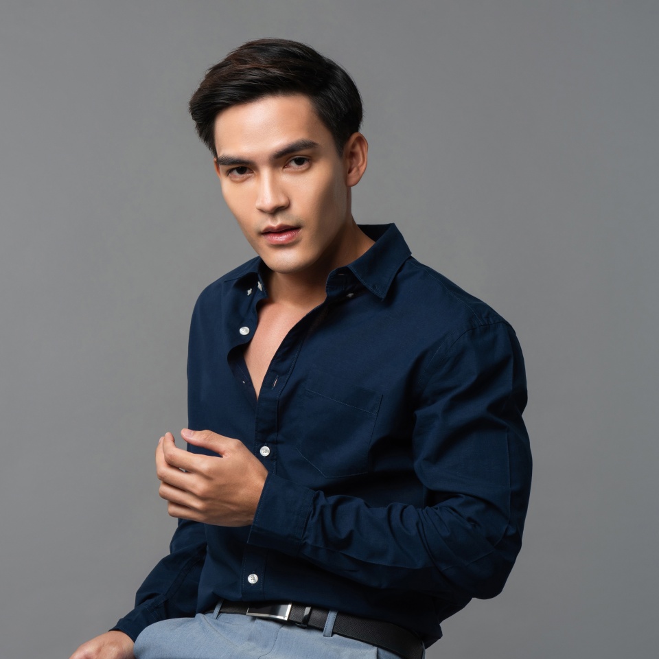 Studio portrait of young sexy handsome Asian man wearing dark blue shirt looking at camera in light gray isolated background