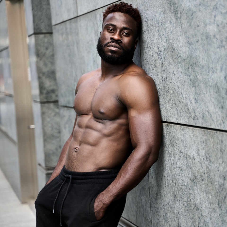 Fit strong sexy shirtless young African man standing at urban wall. Sporty muscular black guy bodybuilder wearing black sport shorts resting after sport street workout training, portrait.