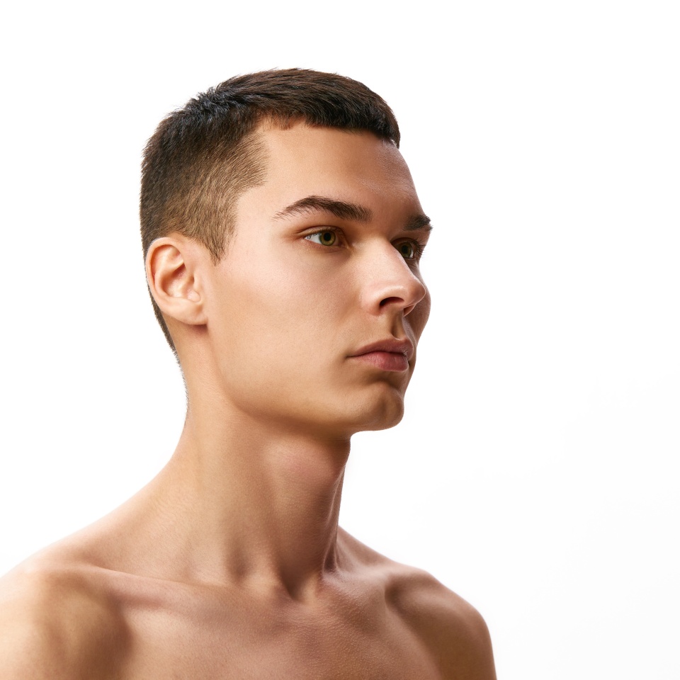 Handsome young brunette man with short hair, spotless perfect skin standing shirtless against white studio background. Concept of male beauty, skin care, spa, cosmetology, men's health