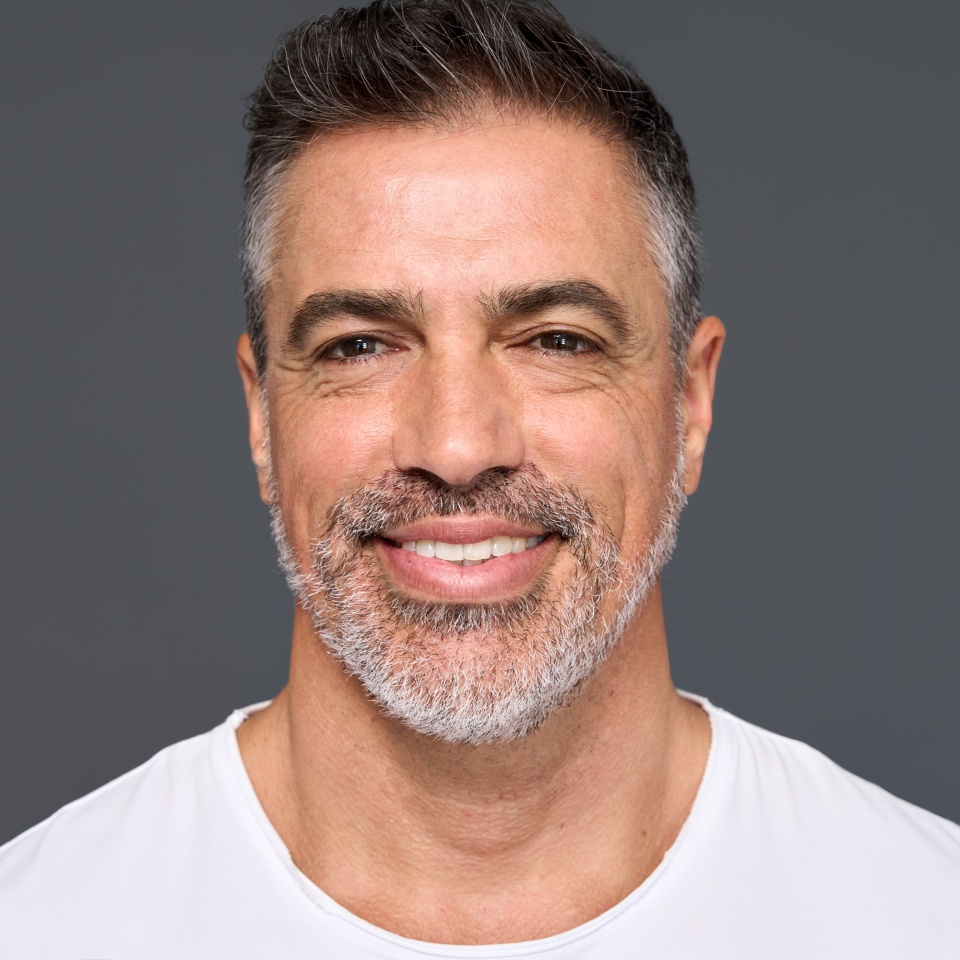 Happy confident handsome healthy mature older man, smiling middle aged male model wearing white t-shirt standing isolated on gray background advertising skin care and dental smile concept.