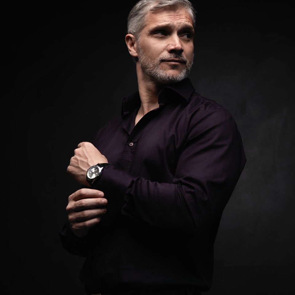 Handsome man posing in black shirt on dark background in studio.