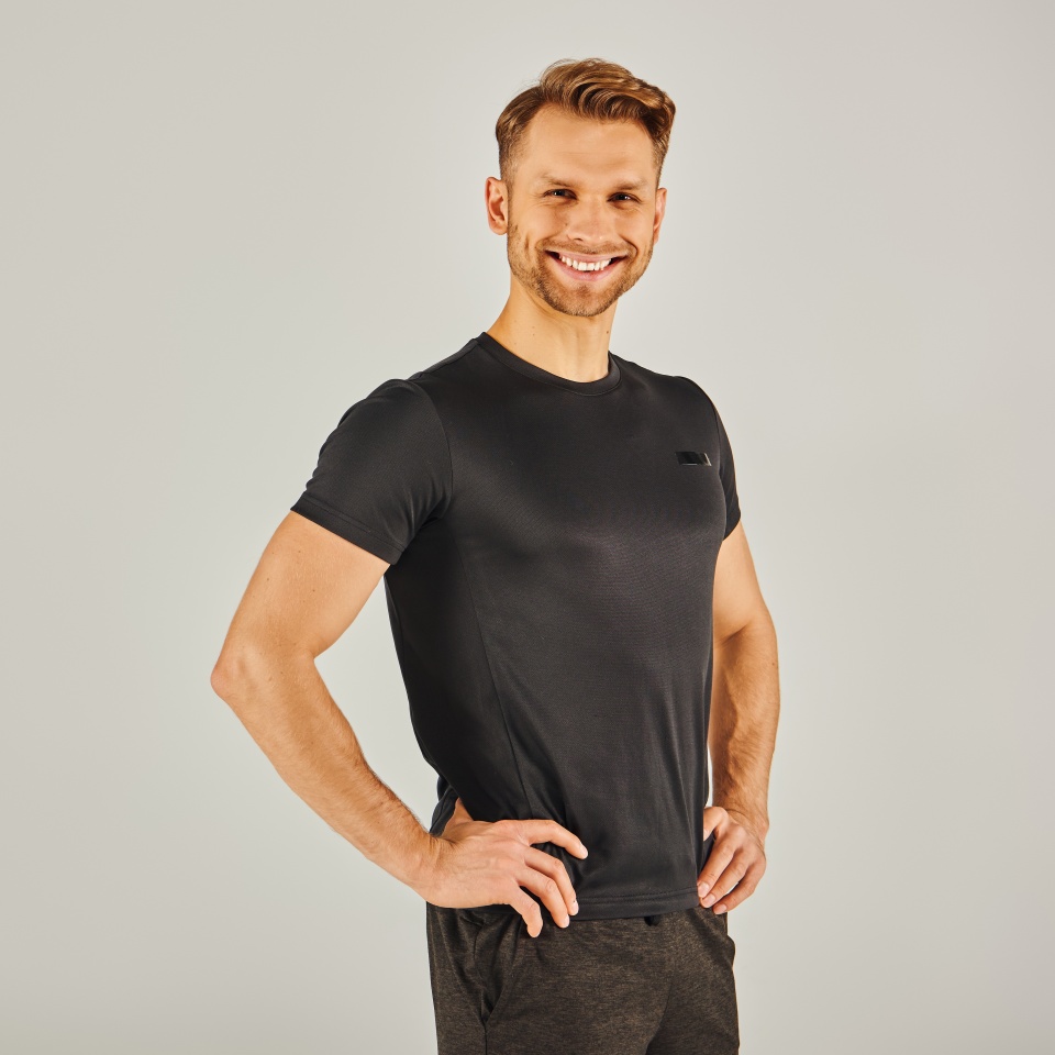 A young athletic man strikes a confident pose while wearing a black t-shirt in a studio setting.