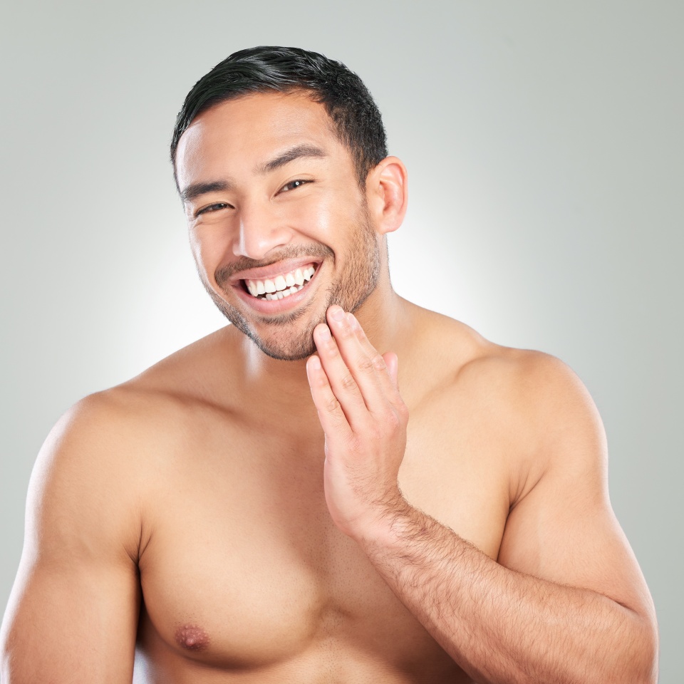 Asian man, skincare and washing face for grooming, hygiene and hydration in studio. Happy, male person and smile with cleaning or facial treatment for wellness and beauty on white background