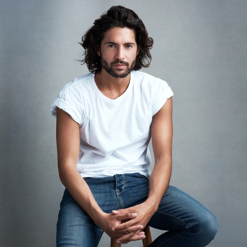 Casual, fashion and portrait of man with confidence, designer clothes and relax on chair in studio. Jeans, pride and cool male model on stool with creative style, trendy aesthetic or grey background
