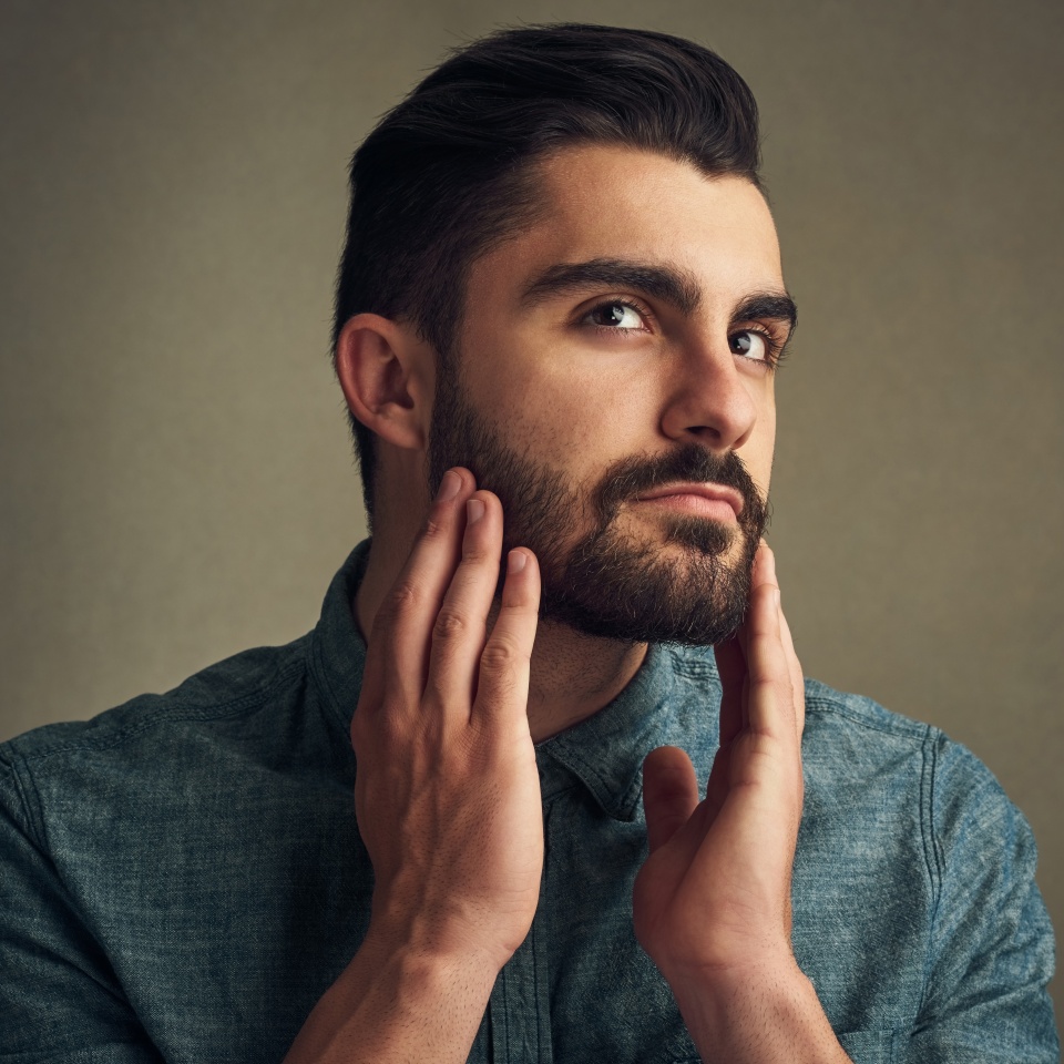 Man, grooming and touch beard on studio background for facial hair maintenance, self care and texture. Male person, growth and personal hygiene on face for skin, beauty and morning routine as barber