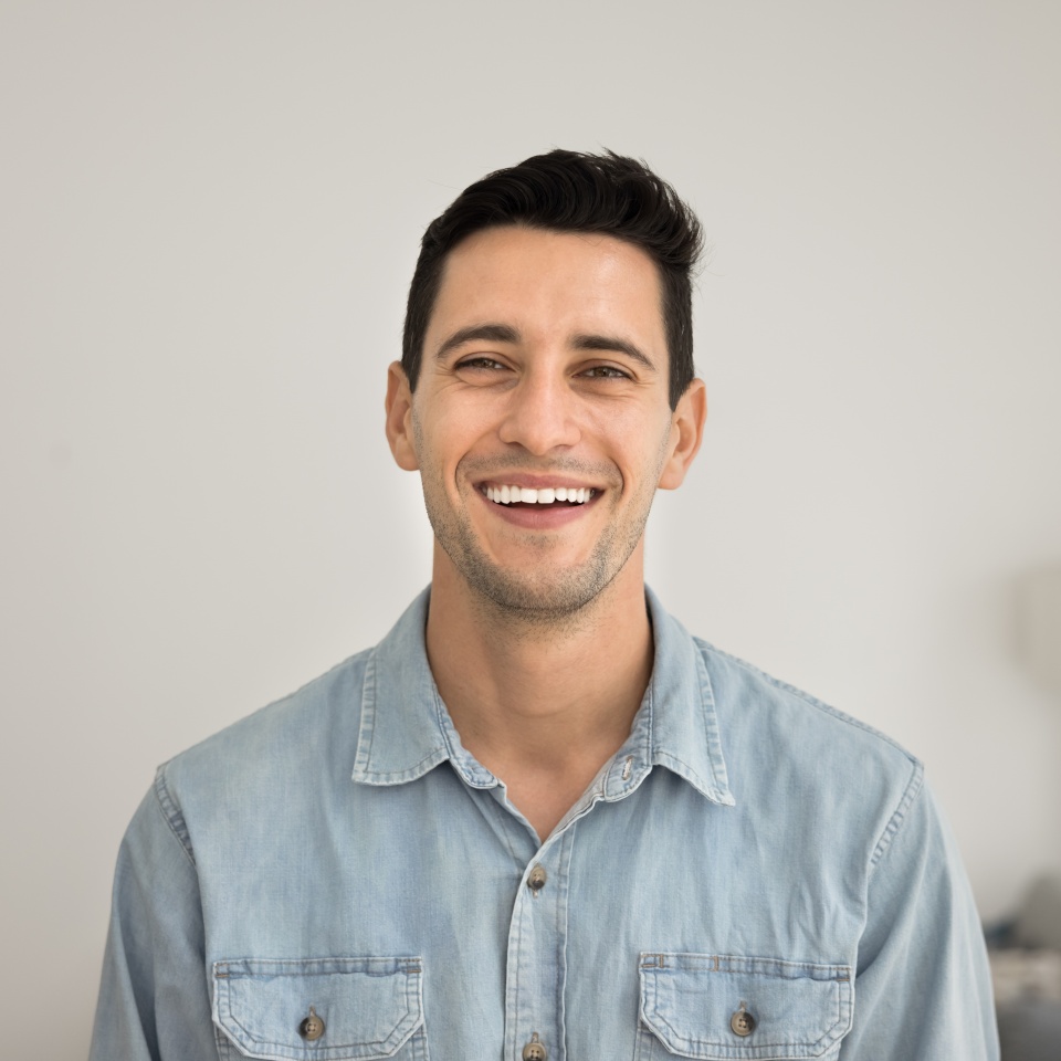 Cheerful attractive brunette Latin man posing for head shot at home, looking at camera with sincere laugh, smiling. Young Hispanic model guy, male homeowner video call screen portrait