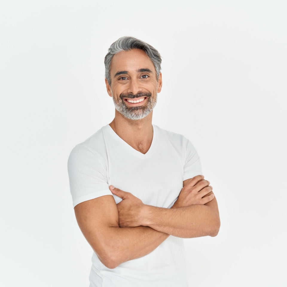 Happy middle aged older man isolated on white studio background. Confident mature mid adult handsome bearded gray-haired male model wearing t-shirt looking at camera with arms crossed. Portrait.