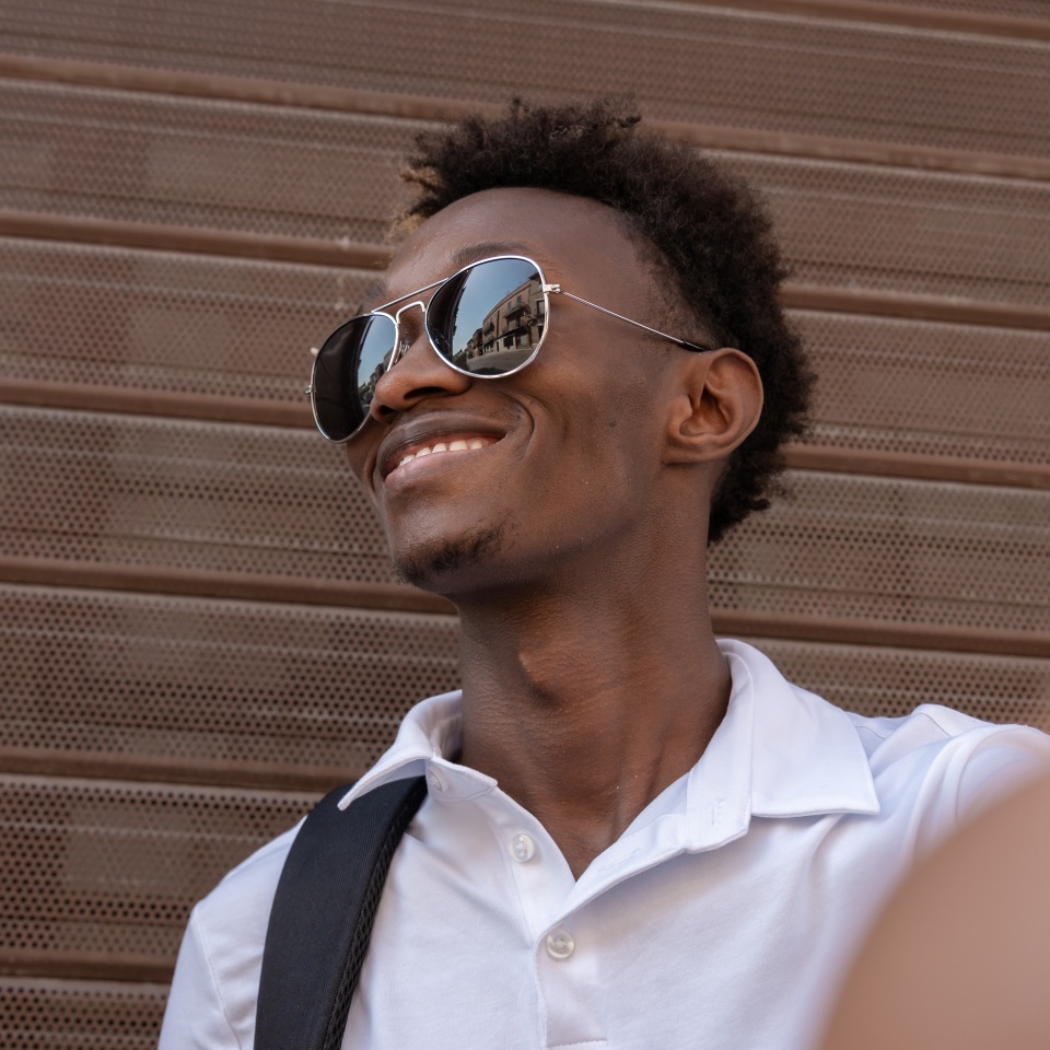 Young man is smiling while wearing sunglasses outside and looking up at something