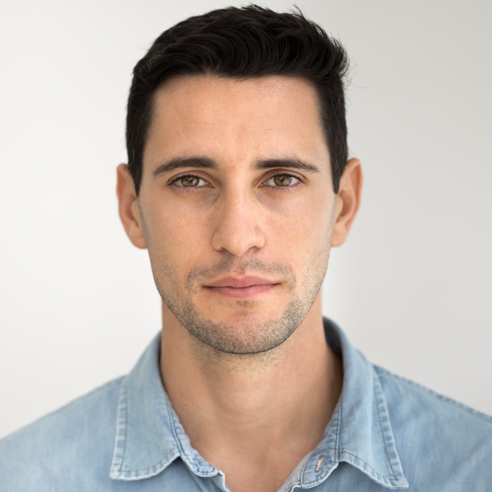Close up head shot portrait of focused handsome Hispanic man dressed in casual denim shirt looking at camera with serious expression, exuding self-assurance, standing on gray studio wall background