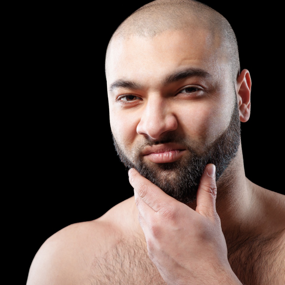 Power and confidence. Close up portrait of strong latino man with beard against black background.